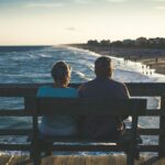 Retired couple sitting on a bench on a pier overlooking a beach