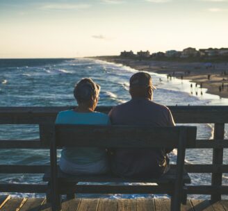 Retired couple sitting on a bench on a pier overlooking a beach