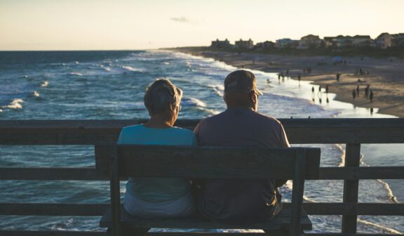 Retired couple sitting on a bench on a pier overlooking a beach