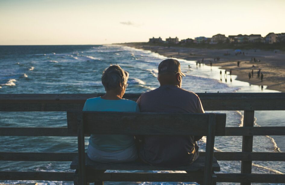 Retired couple sitting on a bench on a pier overlooking a beach