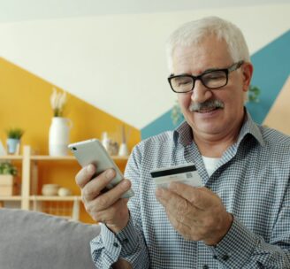 Smiling retired man looking at his mobile phone and credit card